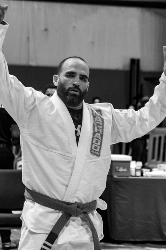 Black-and-white photo of a competitor in a white gi raising both arms after his match.