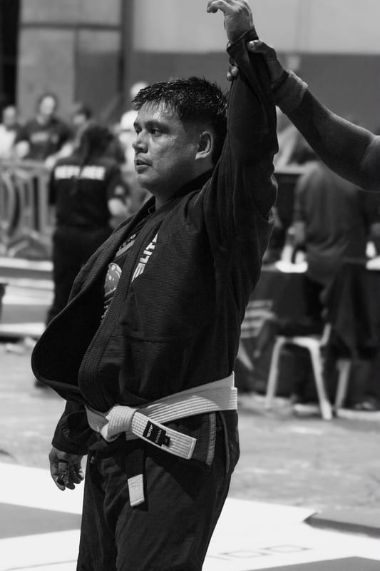 Black-and-white photo of a competitor in a black gi having his hand raised in victory.