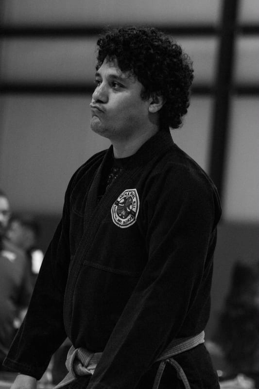 Black-and-white photo of an adult competitor in a black gi waiting matside before his match.