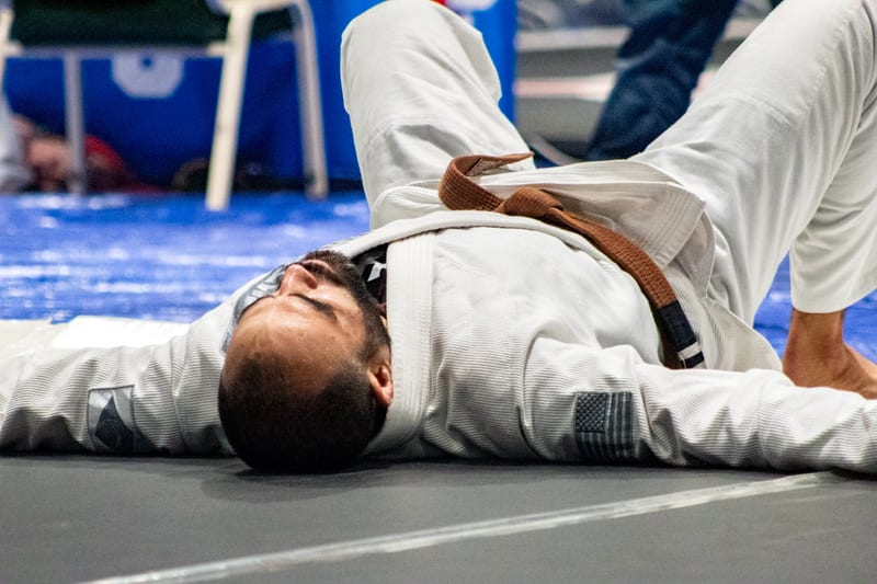 A competitor in a white gi lies back on the mat to recover after a hard match.