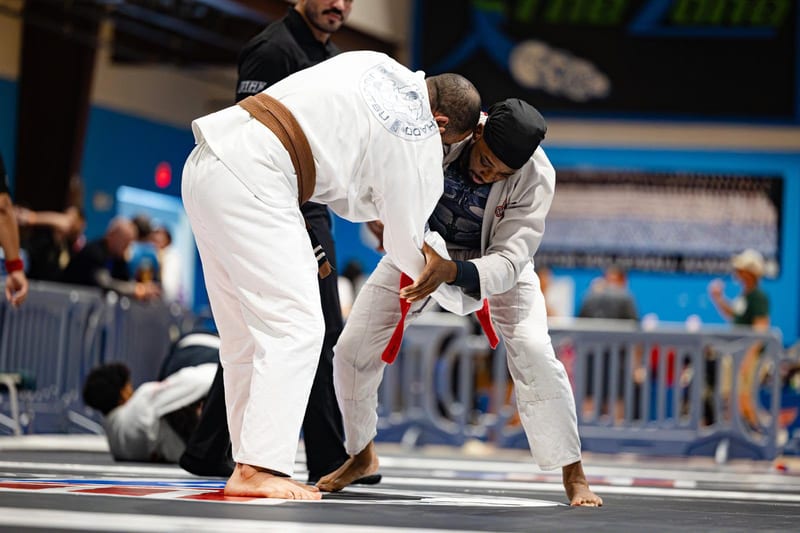 Two competitors in white gis fight for grips standing during an adult gi match.