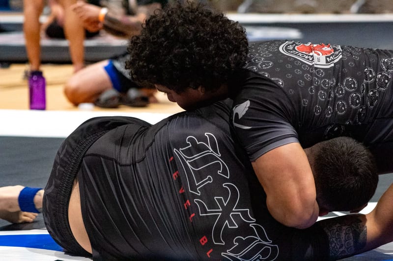 Two competitors in black gis grapple in a tight exchange during a gi match.