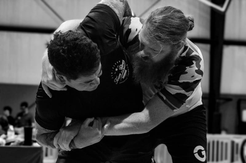 Two no-gi competitors tangle in a standing scramble during an adult match.