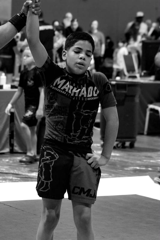 Black-and-white photo of a boy in a Machado rashguard standing ready on the mat.