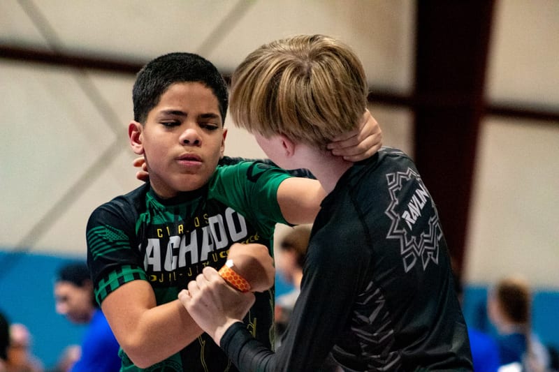Two boys fight for grips standing during a kids no-gi match.