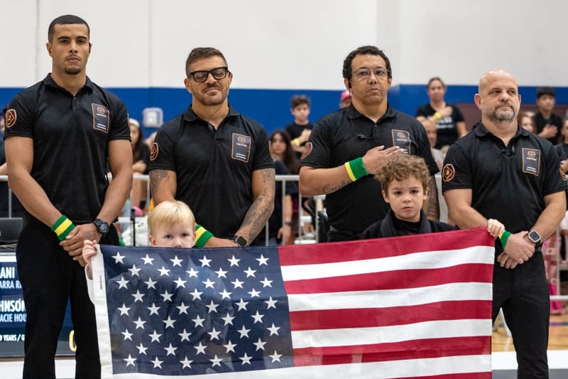 Four coaches stand with two young children holding an American flag during the national anthem.