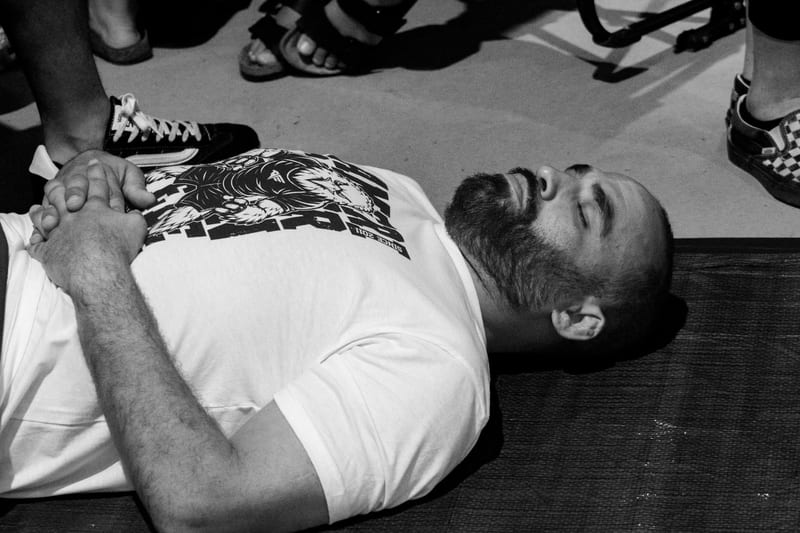 Black-and-white photo of a bearded competitor lying flat on the mat to recover after his match.