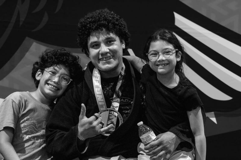 Black-and-white photo of a smiling competitor with a medal posing with two young students at the tournament.