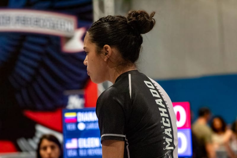 A girl in a Machado rashguard waits matside beside the scoreboard before her match.