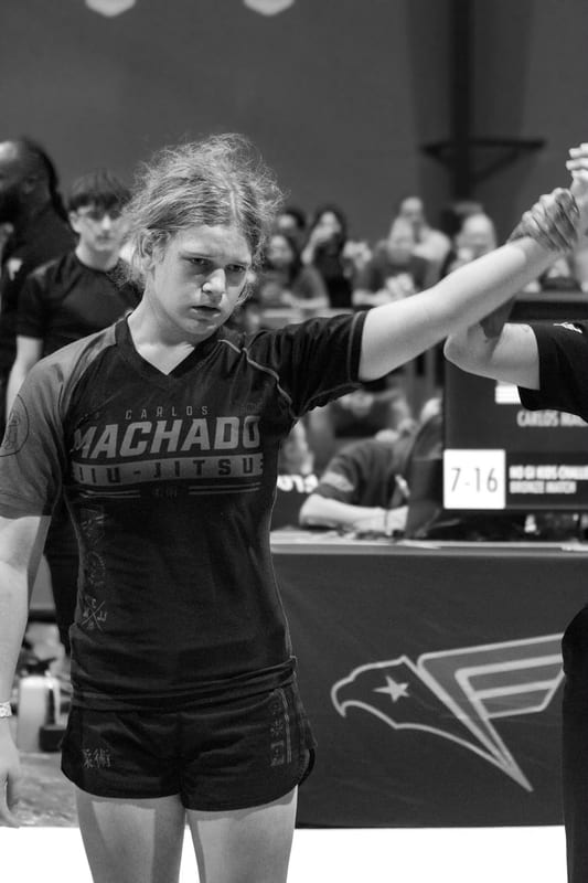 Black-and-white photo of a girl in a Machado rashguard having her hand raised in victory.