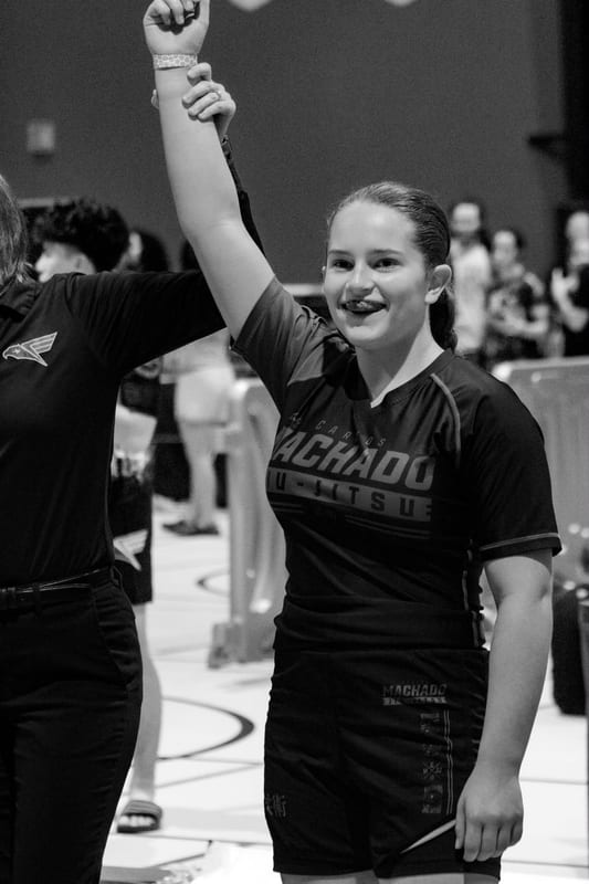 Black-and-white photo of a smiling girl having her hand raised in victory after her match.