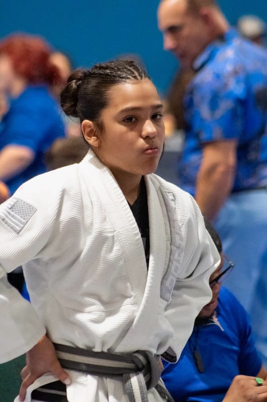 A girl in a white gi stands matside waiting for her match.