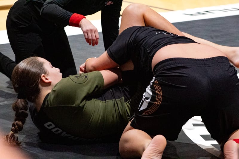 A girl attacks a submission from the bottom during a no-gi match.