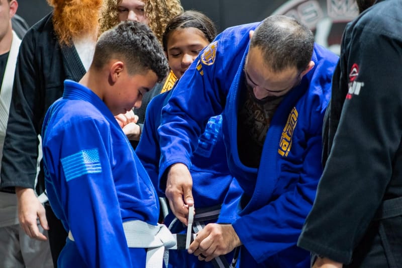 A belt promotion with kids and teens gathered around