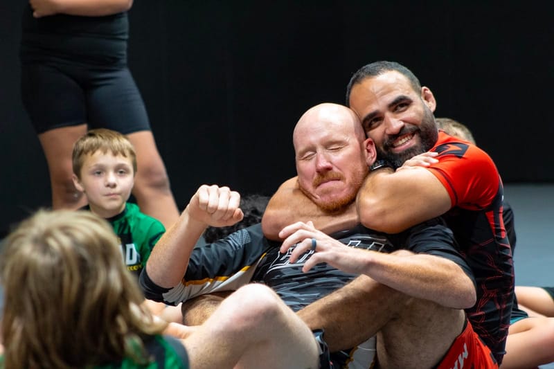 Two training partners embracing after a roll as kids look on