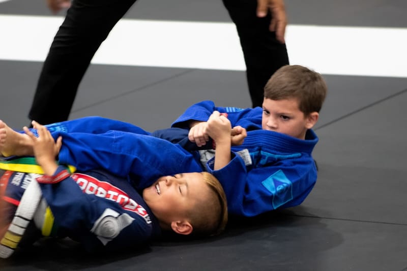 A young boy in a blue gi controls his opponent in a grip fight during a kids competition match.