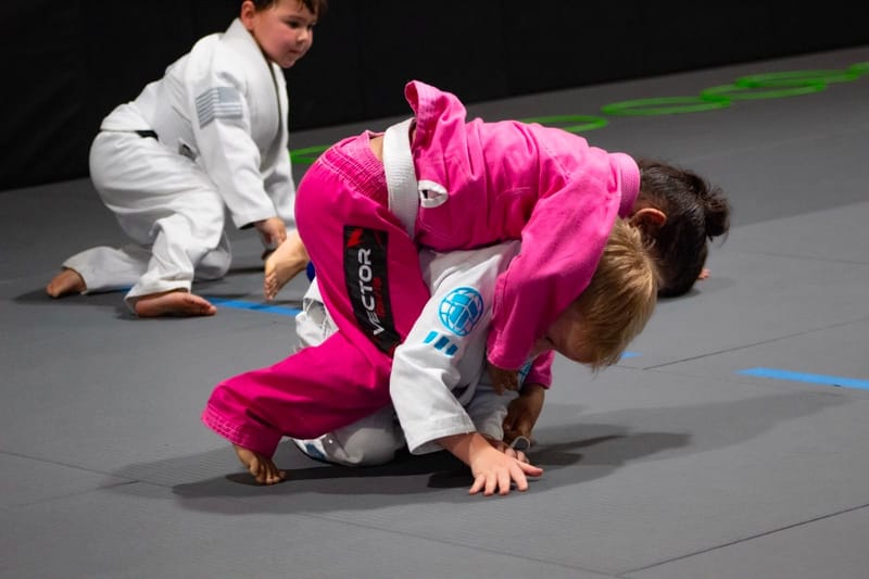 A girl in a pink gi holding mount on a partner