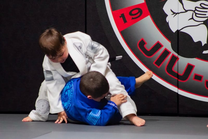 Two young boys sparring in front of the academy logo wall