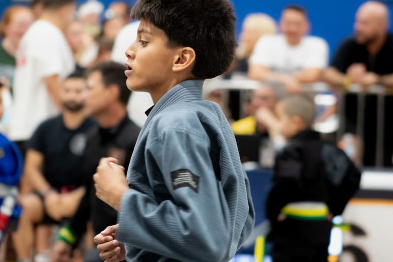 Two small boys in blue and black gis grip up and battle head to head in a standing clinch.