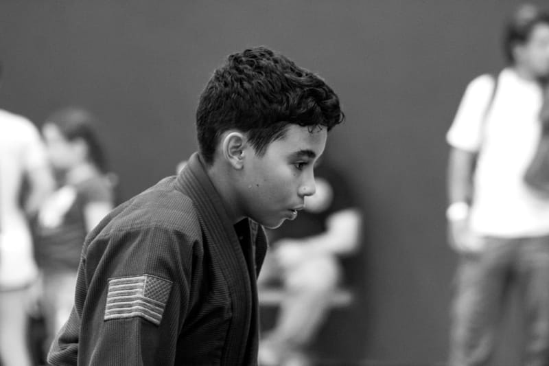 A black-and-white profile portrait of a focused teenage competitor in a gi before a match.