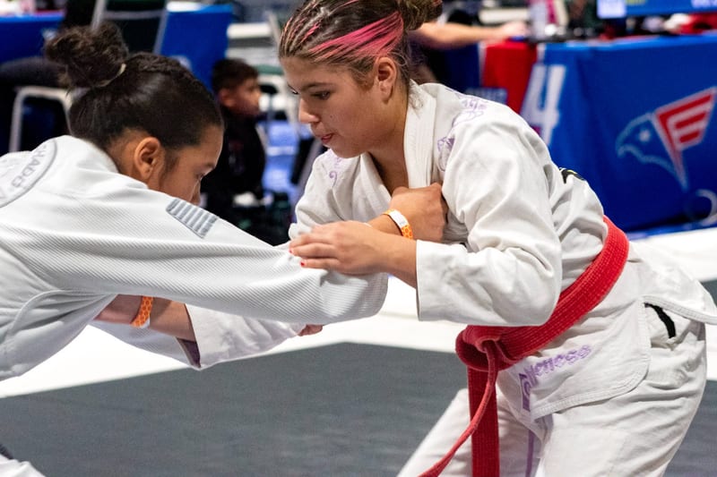Two teen girls in white gis fight for grips at the start of a match.