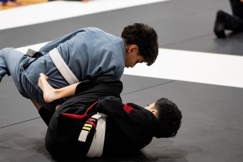 A teen competitor in a light blue gi works to pass his opponent’s guard during a match.