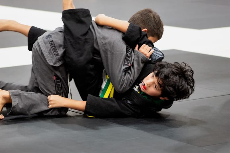 Two boys scramble for control on the mat during a gi jiu-jitsu tournament match.