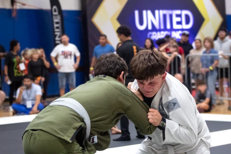 Two teenage competitors clinch on the feet in front of a United Grappling backdrop.