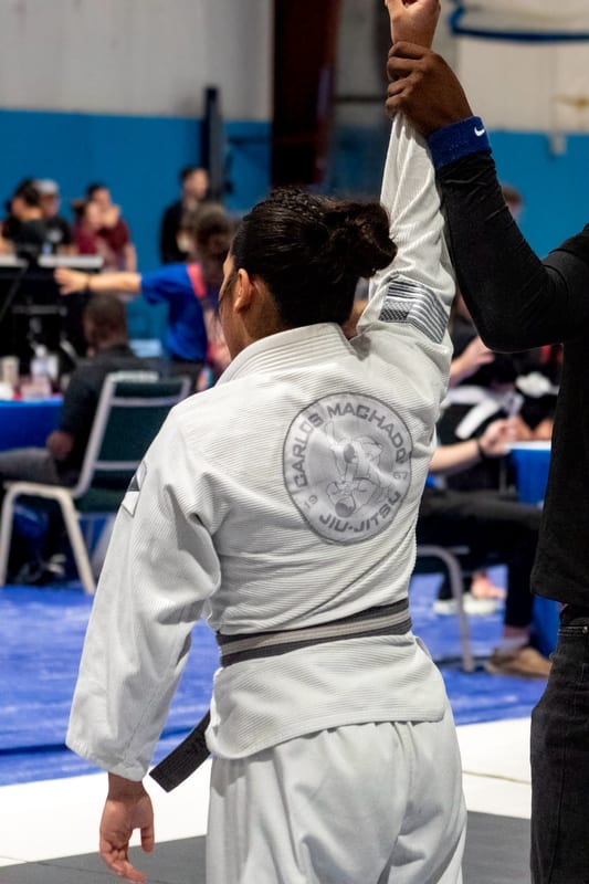 A woman in a white gi has her hand raised in victory after her match.