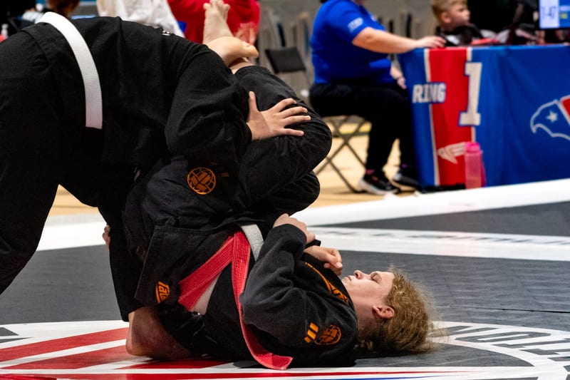 A woman in a black gi works from closed guard during a women's gi match.