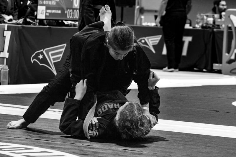 Black-and-white photo of a woman in a gi controlling her opponent from the top.