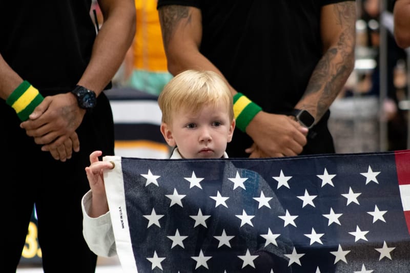 A small child in a white gi holds an American flag during an event opening ceremony.