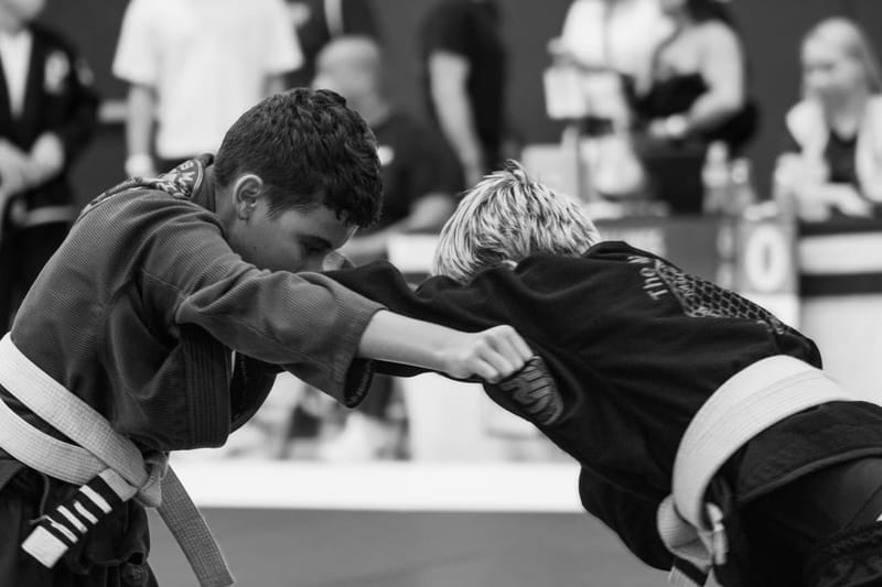Black-and-white photo of two boys in gis locked in a standing clinch during a jiu-jitsu match.
